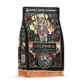 The front of a 12 ounce bag of Bones Coffee Company Colombia single-origin coffee. It is a medium roast, and it has a donkey with bags of coffee on its back and flowers around it on the art.