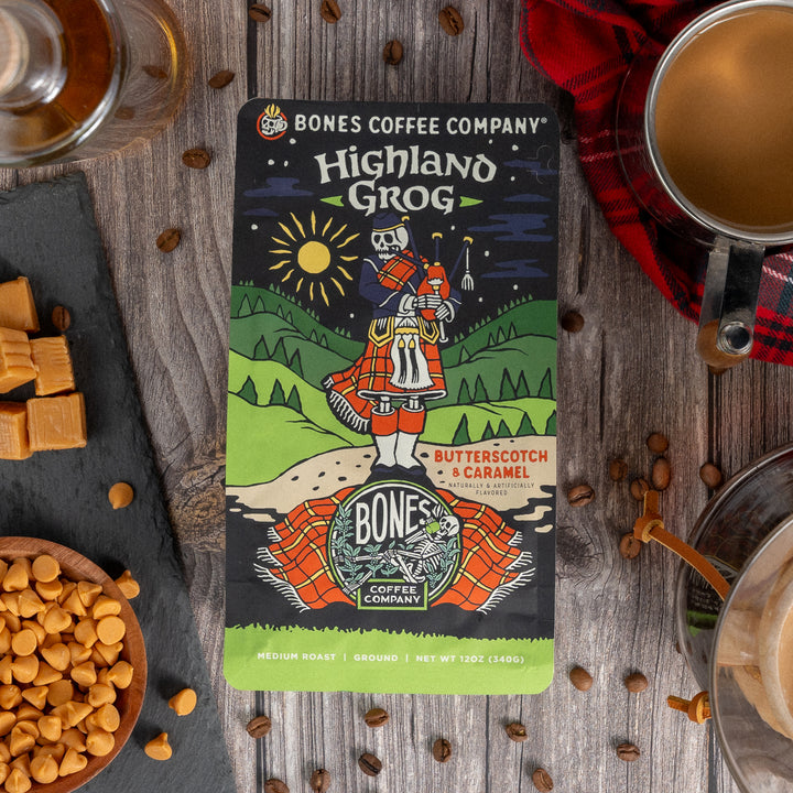 Bones Coffee Highland Grog bag with butterscotch caramel flavor, surrounded by coffee beans, caramel pieces, and a cup.